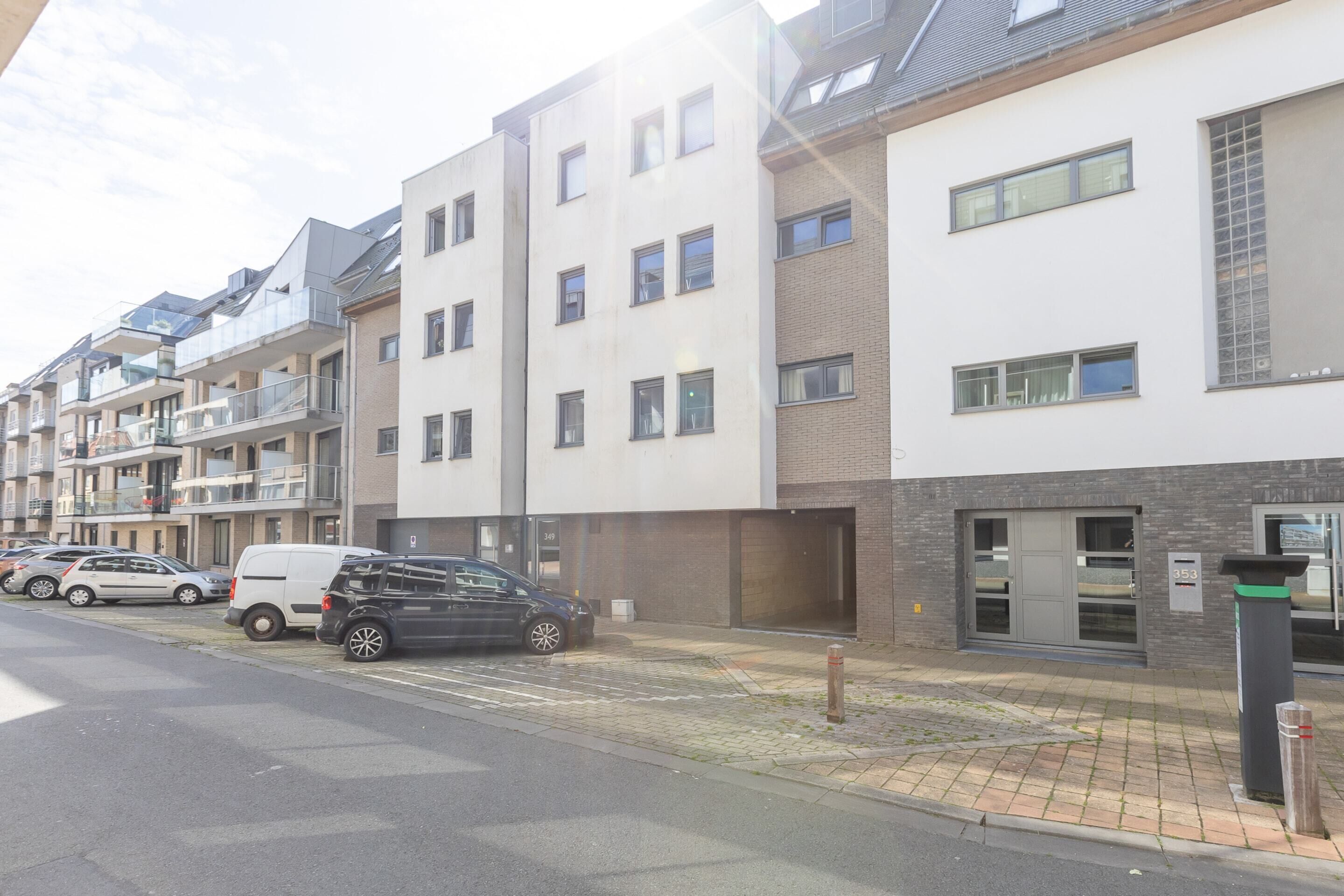 Une rangée d’immeubles résidentiels modernes à plusieurs étages, dotés de balcons, d’un espace de stationnement et d’une entrée bien visible menant à l’immeuble numéro 353.