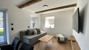 Un soggiorno moderno con un divano grigio, un tavolino in legno e una poltrona grigia. C'è una TV montata a parete e una finestra che offre luce naturale.