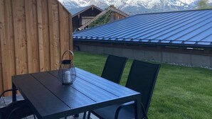 Un muro esterno in legno, un tavolo con sedie e vista sulle montagne innevate.