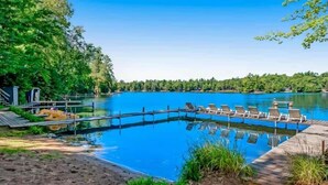 A swimming pool with lounge chairs and a wooden deck, surrounded by trees and a clear blue sky.
