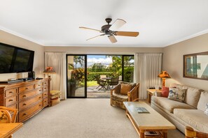Amplia sala de estar con televisión de pantalla plana, muebles de madera, ventilador de techo y puerta corrediza de vidrio que da a un patio exterior.