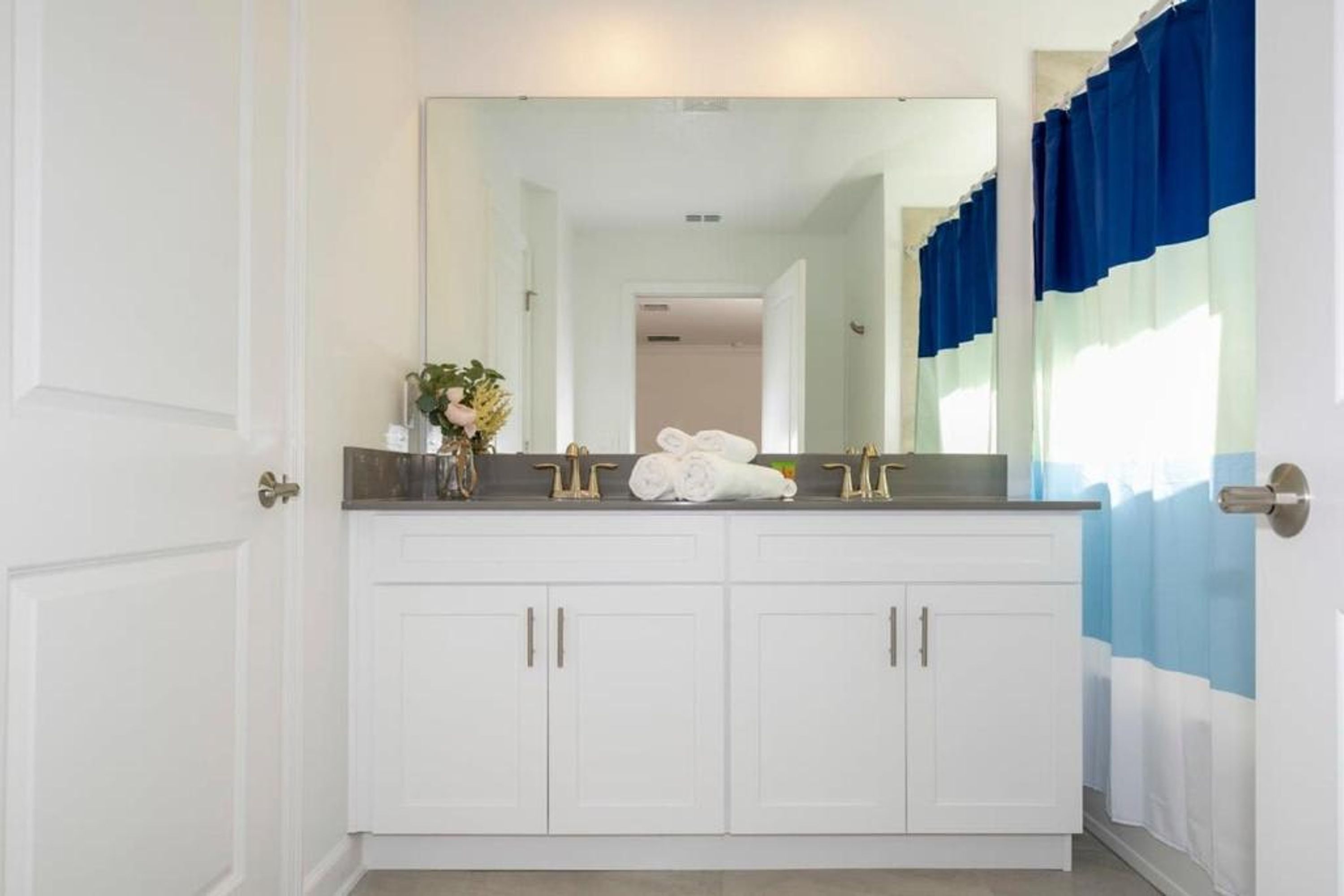A bathroom with white cabinets, a large mirror, and a towel rack.