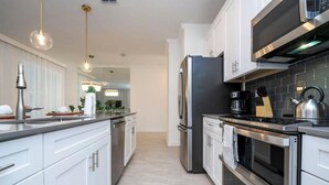 A modern kitchen with white cabinets, stainless steel appliances, and pendant lighting. - 2557 Awesome 4BD Townhouse Located at Storey Lake (Kissimmee)