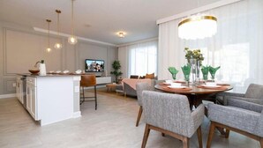 A modern kitchen with a central island, a dining area with grey upholstered chairs, and a large window with sheer curtains. - 2557 Awesome 4BD Townhouse Located at Storey Lake (Kissimmee)