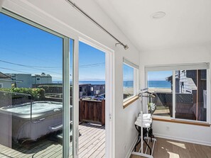 A modern bathroom with a glass door leading to a deck, a hot tub, and a view of the ocean.