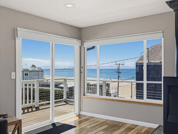 A room with a large sliding glass door leading to a balcony with a view of the sea and buildings.
