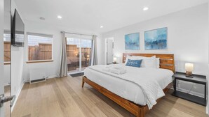 Une chambre à coucher avec un lit en bois, du linge de lit blanc, une table de chevet avec une lampe et deux tableaux abstraits accrochés au mur.