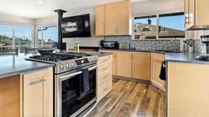 Une cuisine moderne dotée d’un grand îlot central, d’appareils électroménagers en acier inoxydable, de meubles de rangement en bois et d’une grande fenêtre offrant une vue dégagée.