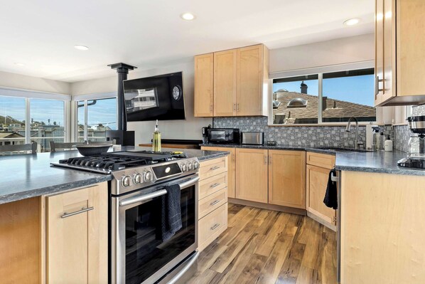 A modern kitchen with a large island, stainless steel appliances, wooden cabinets, and a large window offering a view. - Pacific Paradise steps from the Beach! (Santa Cruz)