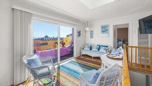 A bright room with a large window, a white sofa, wicker chairs, and a colorful striped rug.
