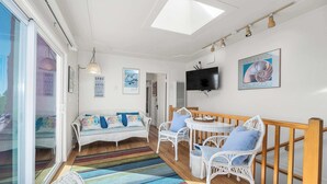 A bright room with a sofa, chairs, a table, and a TV on the wall.