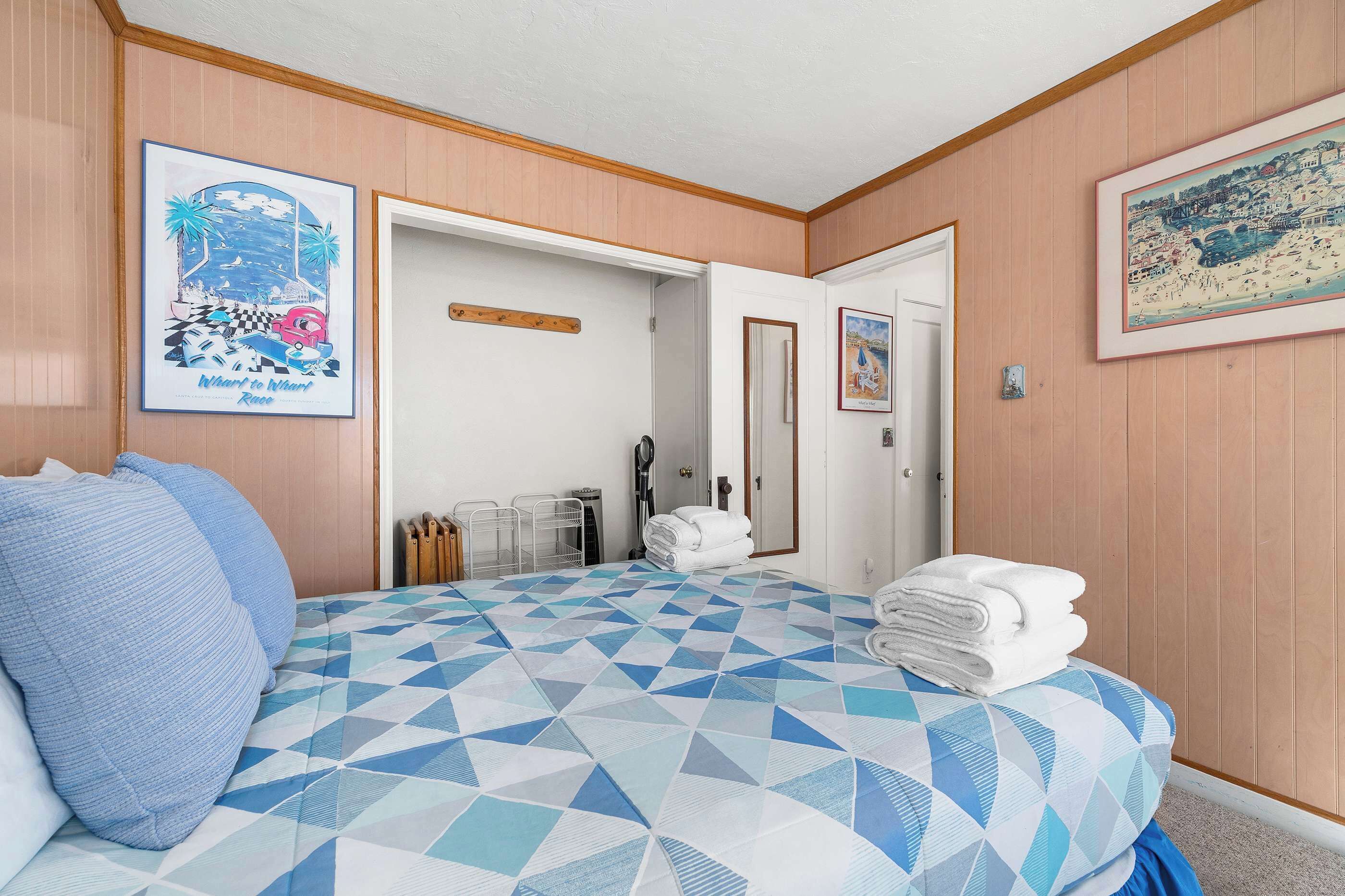 A hotel room with a bed, pillows, a towel stack, a door, and two framed pictures on the wall.