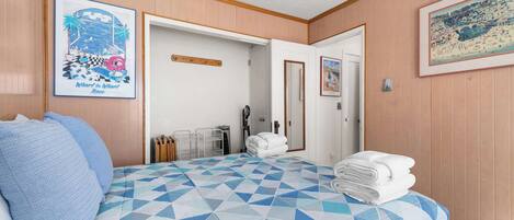 A hotel room with a bed, pillows, a towel stack, a door, and two framed pictures on the wall.