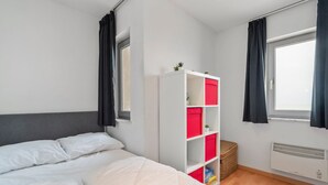 A bedroom with a bed, a white wardrobe with red storage compartments, a window with curtains, and an air conditioning unit. - One-bedroom Flat With sea Views and Parking (Blankenberge)