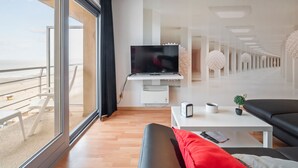 A modern living room with a large TV, a coffee table, a sofa, and a view of the beach. - One-bedroom Flat With sea Views and Parking (Blankenberge)