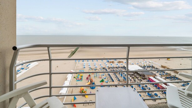 A beach view from a balcony with a railing, featuring a sandy beach, umbrellas, and beach chairs. - One-bedroom Flat With sea Views and Parking (Blankenberge)