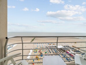 A beach view from a balcony with a railing, featuring a sandy beach, umbrellas, and beach chairs. - One-bedroom Flat With sea Views and Parking (Blankenberge)