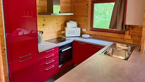 A compact kitchen with wooden walls, a red cabinet, a microwave, a stove, and a window with curtains. - Cozy Vacation Home, Namur (Viroinval)