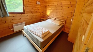 A wooden cabin bedroom with a bed, a nightstand, a window, and a picture of a deer on the wall. - Cozy Vacation Home, Namur (Viroinval)
