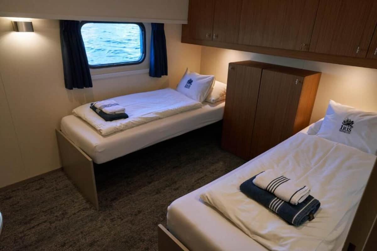 A small cabin with two single beds, a wooden cabinet, and a window with curtains.