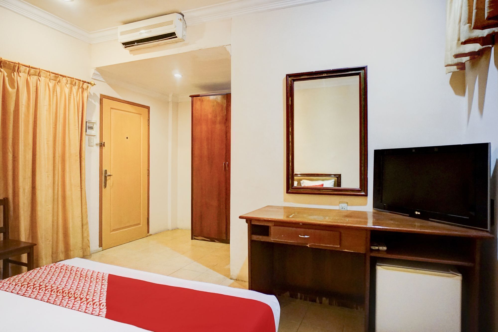 A hotel room with a bed, a desk with a mirror, a television, and a wardrobe.