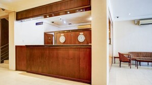 Egy fa borítású recepciós pult, két falióra és egy tábla, amely a pénztár helyét jelzi.