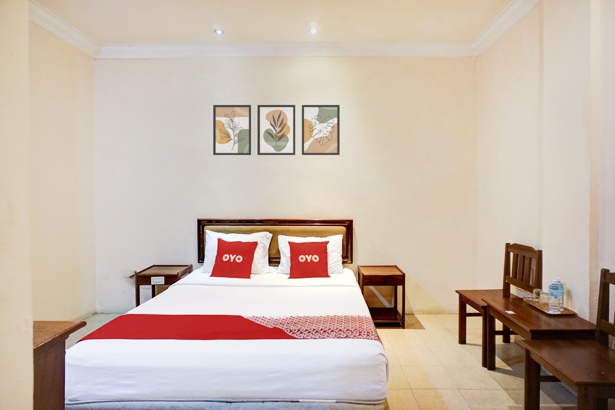 Una camera d'albergo con un letto grande, due comodini, una sedia di legno e tre opere d'arte appese al muro.