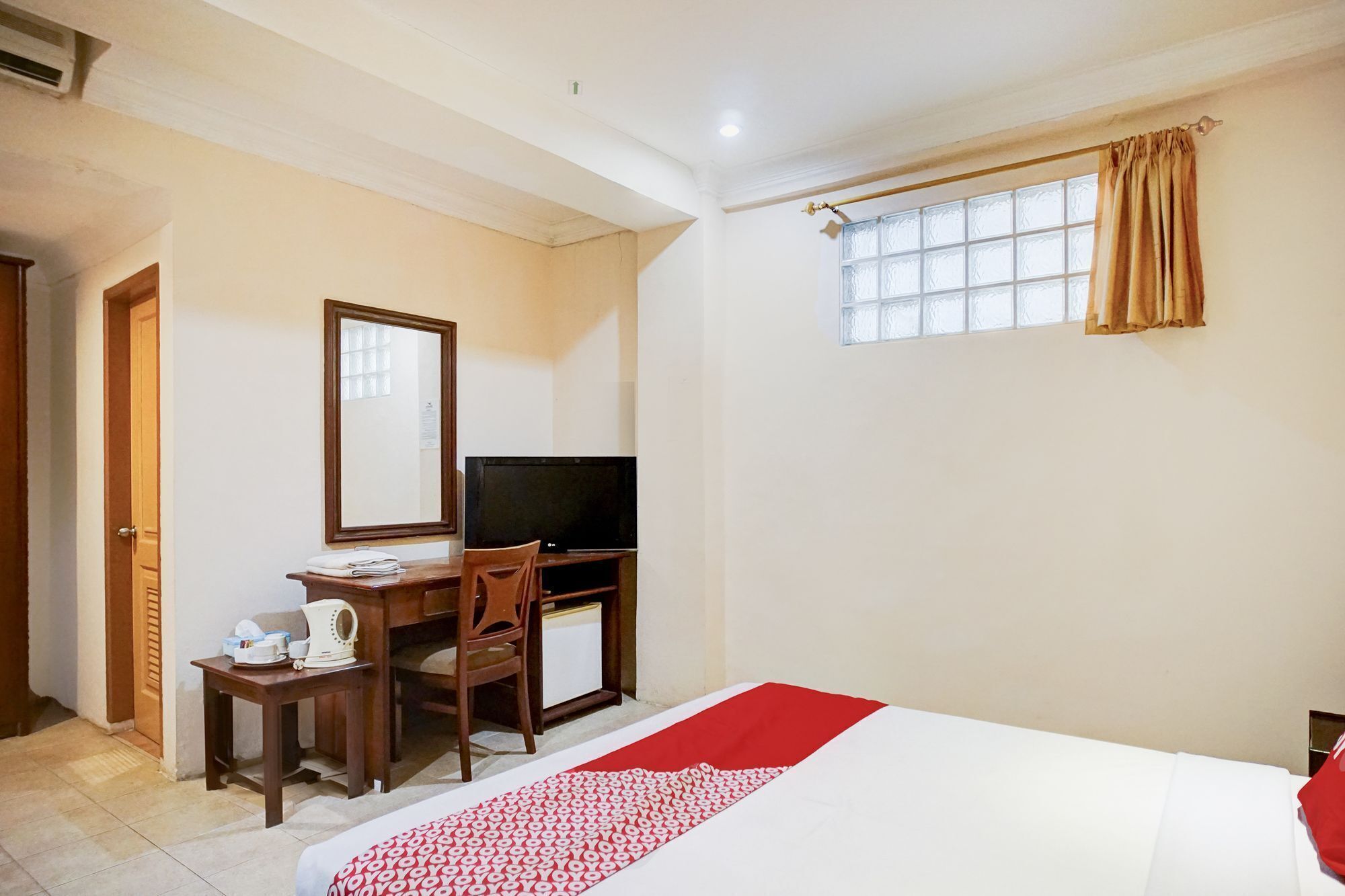 A hotel room with a bed, a desk with a computer, a chair, a mirror, and a window with curtains.