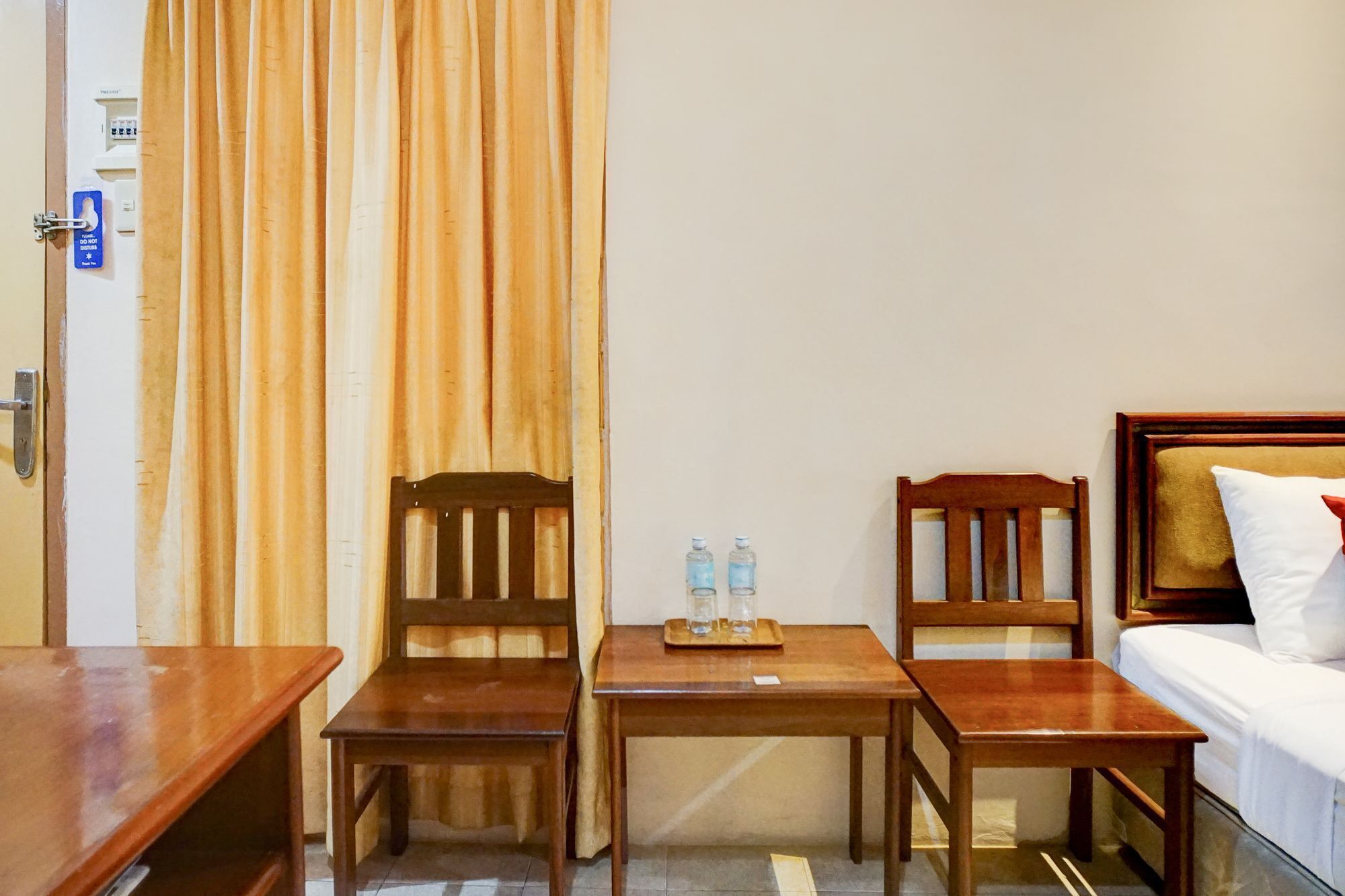 Hotelkamer met een bed, twee houten stoelen, een tafeltje met waterflesjes en een deur met een ‘Niet storen’-bordje.