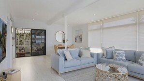 Una sala de estar moderna con un sofá azul claro, una mesa de centro redonda y un ventanal corredero que da a un balcón.