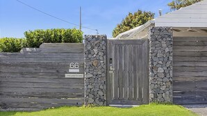 Una entrada protegida con un muro de piedra y una valla de madera, un letrero con el número '66', y un cartel sobre el portón que dice 'THE LAKE ESCAPE'.