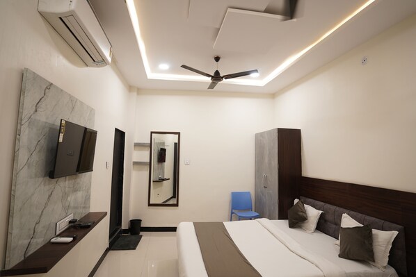 A modern hotel room with a bed, a TV, a ceiling fan, and a marble wall. - Hotel Dev kripa (Ujjain)