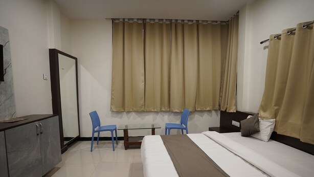 A hotel room with a bed, two chairs, a small table, a mirror, and a window with curtains. - Hotel Dev kripa (Ujjain)