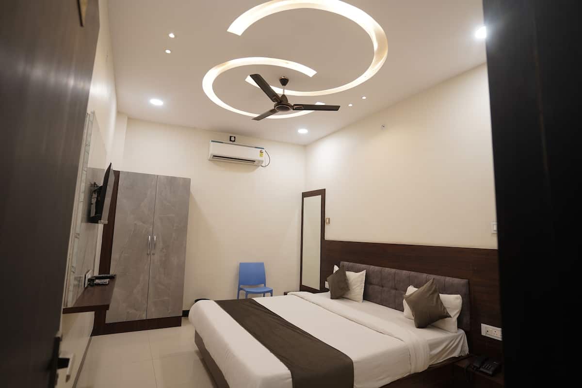 A modern hotel room with a large bed, a ceiling fan, recessed lighting, a built-in air conditioning unit, and a bedside telephone.