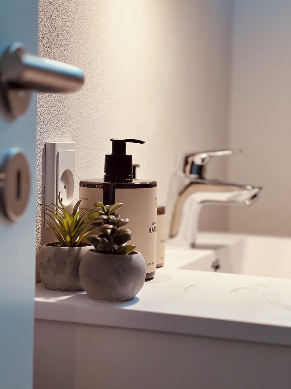 A bathroom with a white sink, a black soap dispenser, and two small potted plants on the counter. - Cozy Flats Silkeborg - 1TH (Silkeborg)