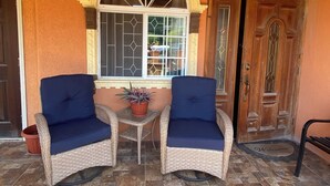 Deux chaises en osier avec des coussins bleus, une petite table et une plante en pot devant une fenêtre ornée d’un panneau de verre décoratif.