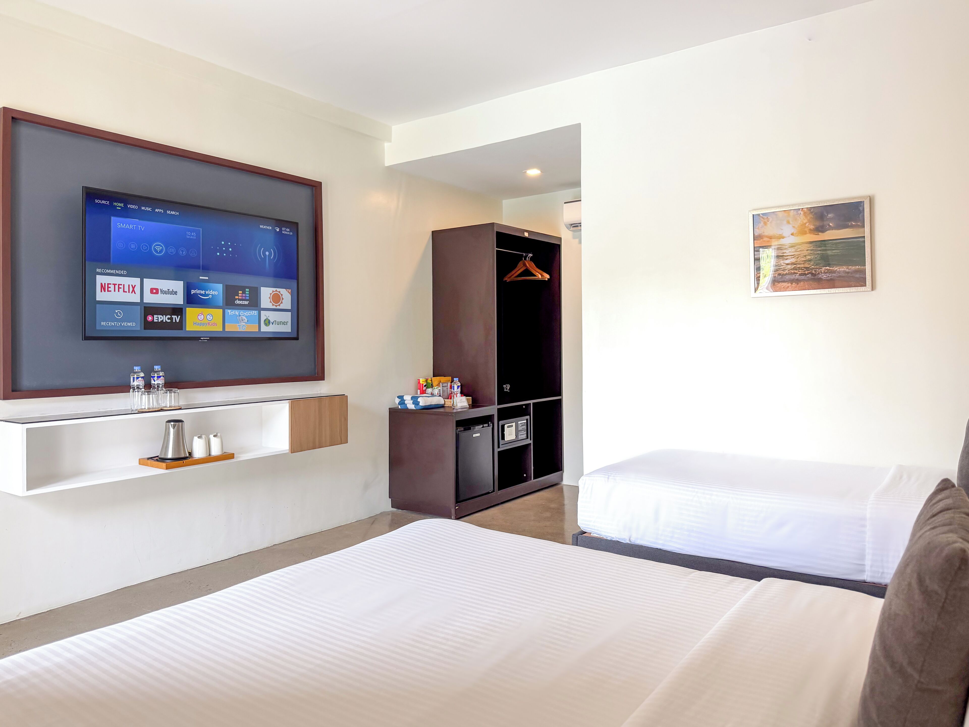A hotel room with a bed, a TV mounted on the wall, a wardrobe, and a painting on the wall.