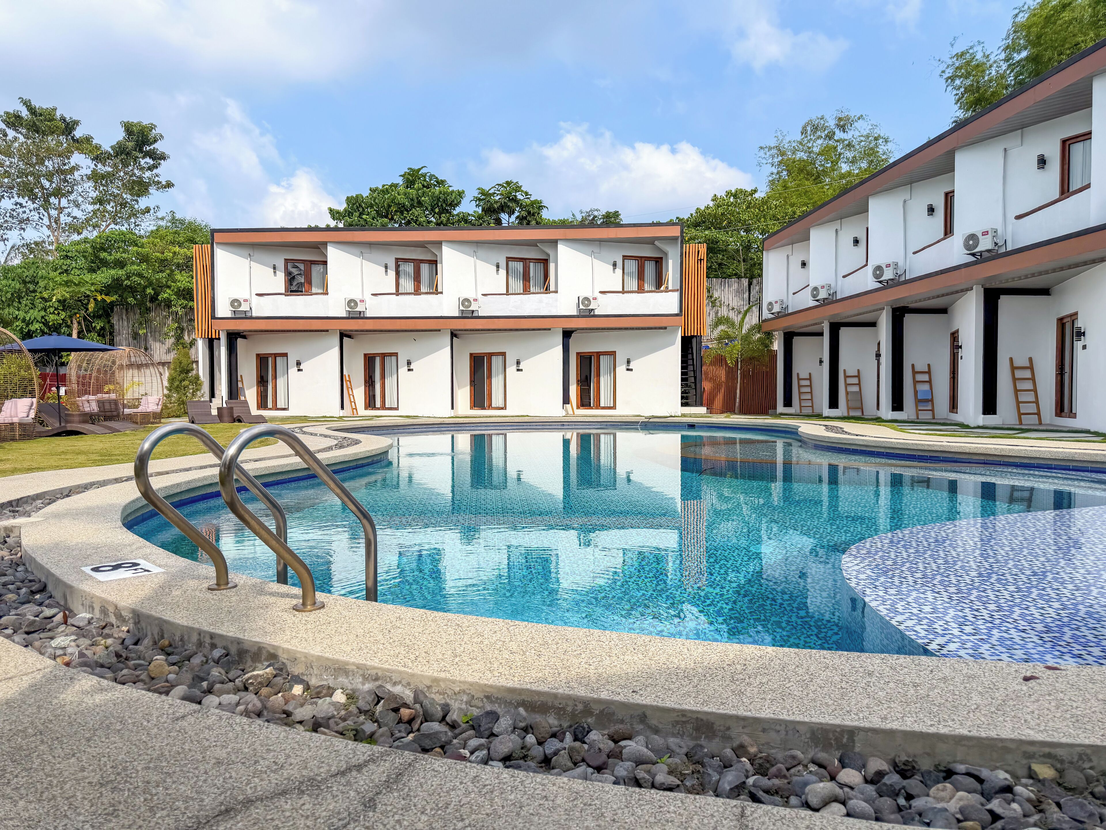 A modern hotel with a swimming pool, outdoor seating, and a two-story building.
