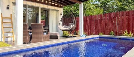 A swimming pool with a pergola, wicker furniture, and a hanging chair.
