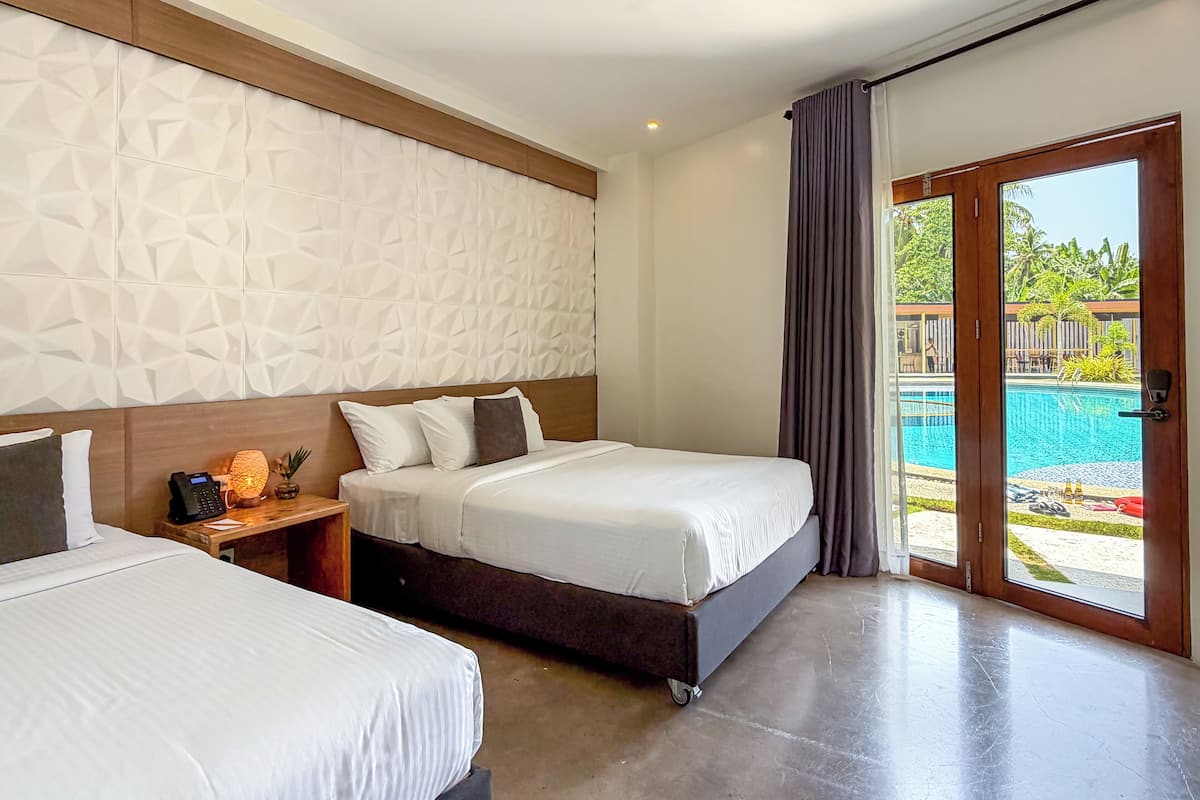 Ein Hotelzimmer mit zwei Betten, einem Holzkopfstück, einer strukturierten Wand, einem Nachttisch mit Lampe und Blick auf einen Außenpool.