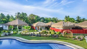 Ein Resort mit strohgedeckten Hütten, einem Swimmingpool und üppiger Vegetation.