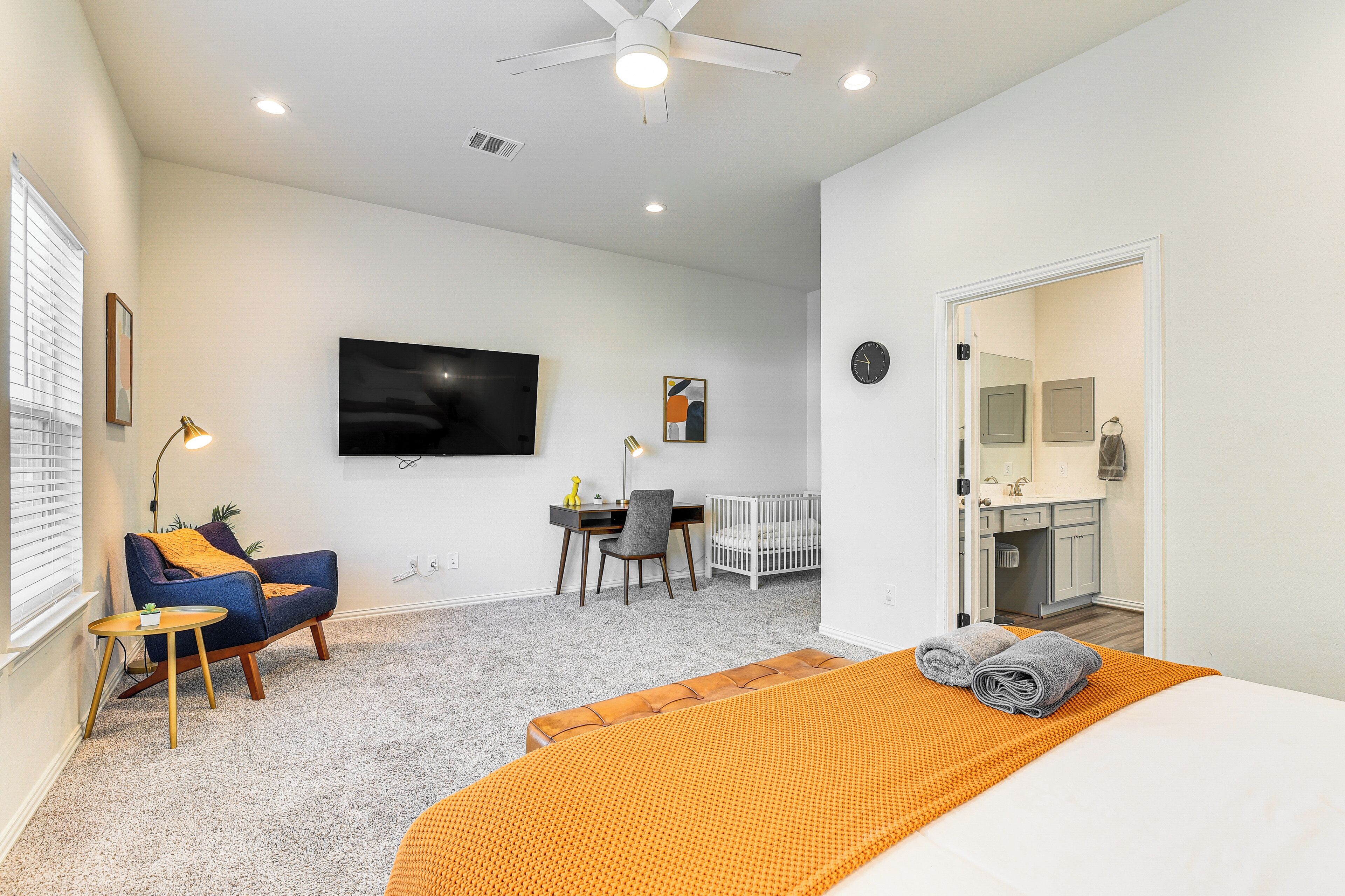 A modern bedroom with a bed, a desk, a chair, a crib, and a television.