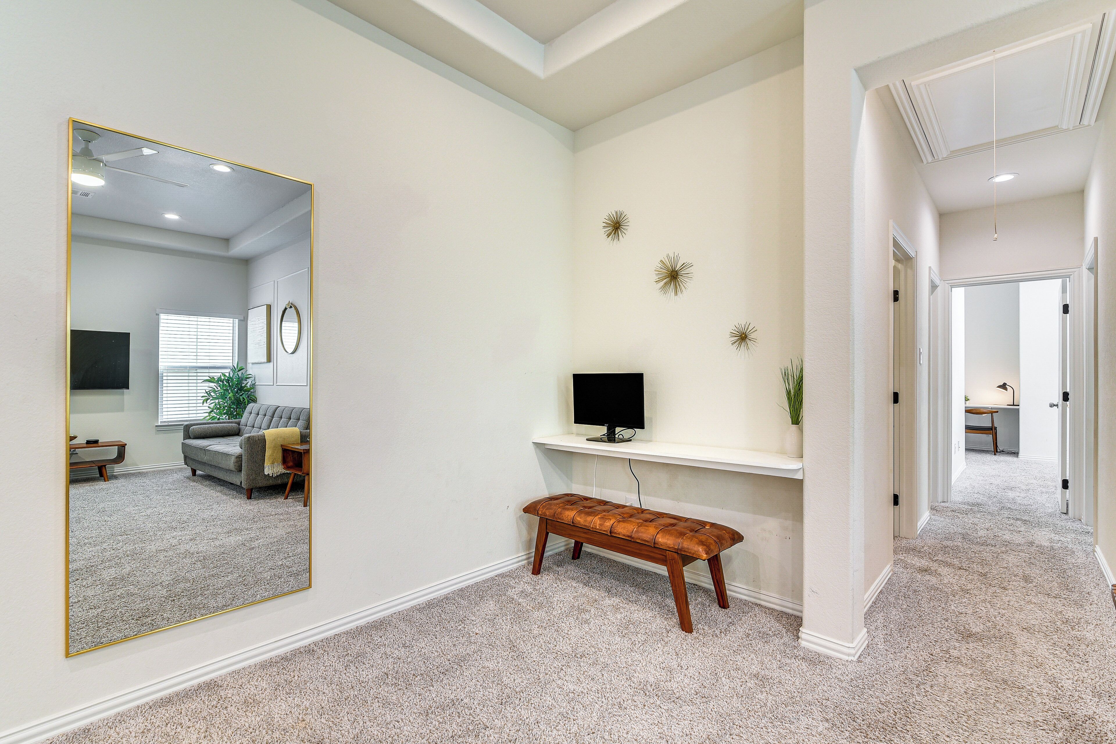 Un pasillo con un banco, un espejo, un televisor en un estante y una puerta que da a otra habitación.