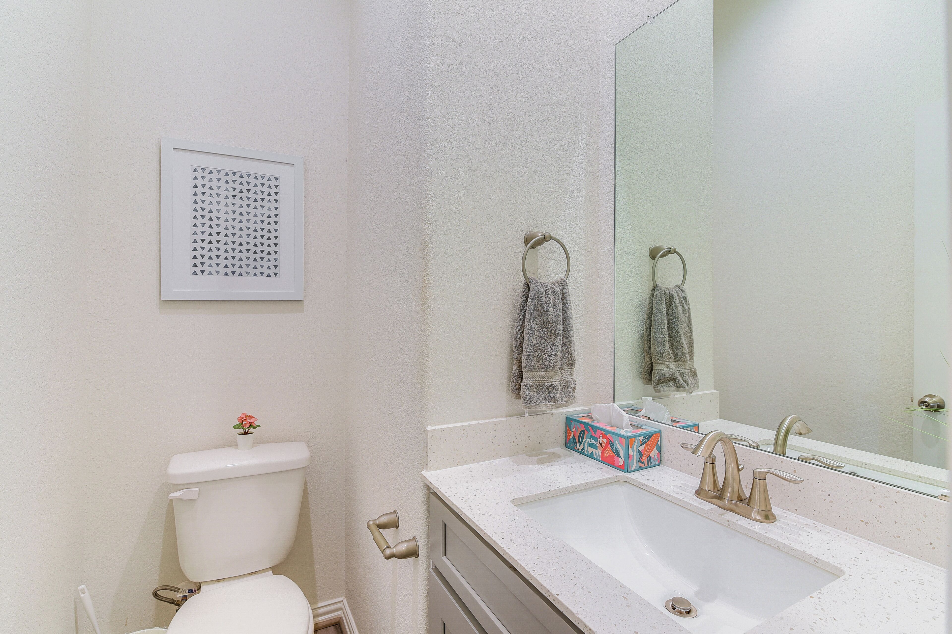 Une salle de bain avec des toilettes blanches, un lavabo avec un miroir et un tableau encadré au mur.