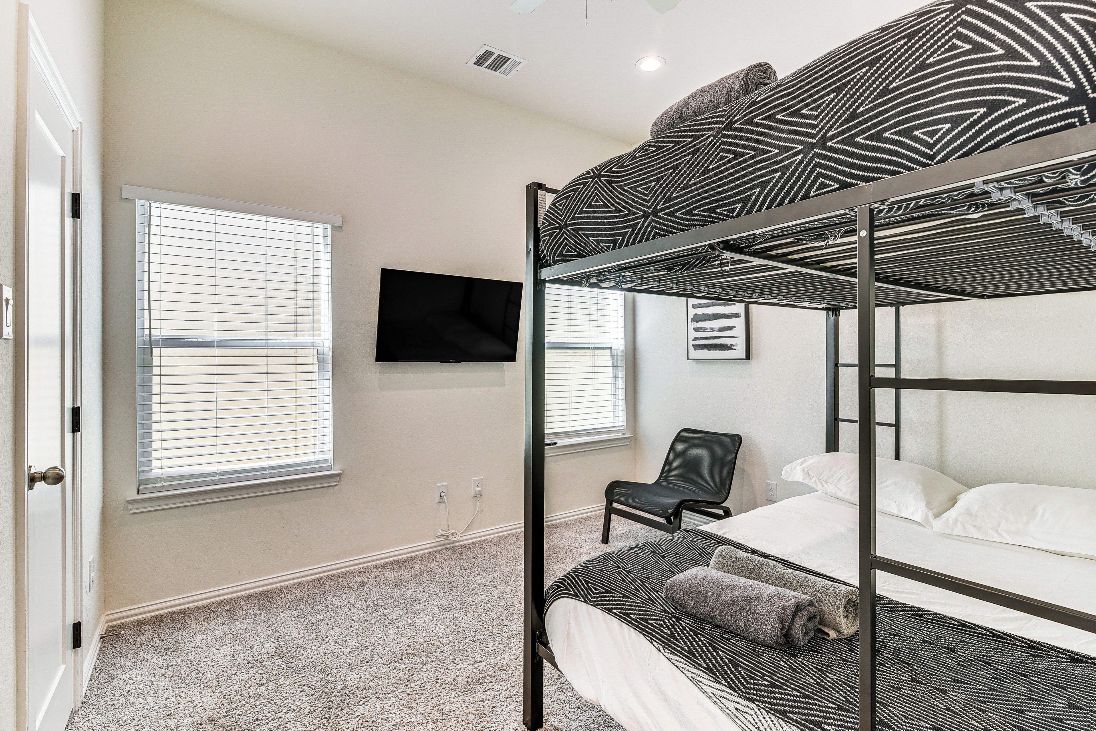 A bunk bed room with a television on the wall, a chair, and a window with blinds.