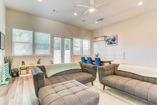 A modern living room with a sectional sofa, a dining area, and large windows with blinds. - 5 Mi to Downtown - Chic Home w/ Patio in Houston! (Houston)