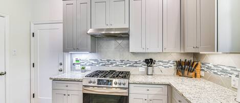 Una cocina con armarios blancos, estufa de acero inoxidable y salpicadero de azulejos.
