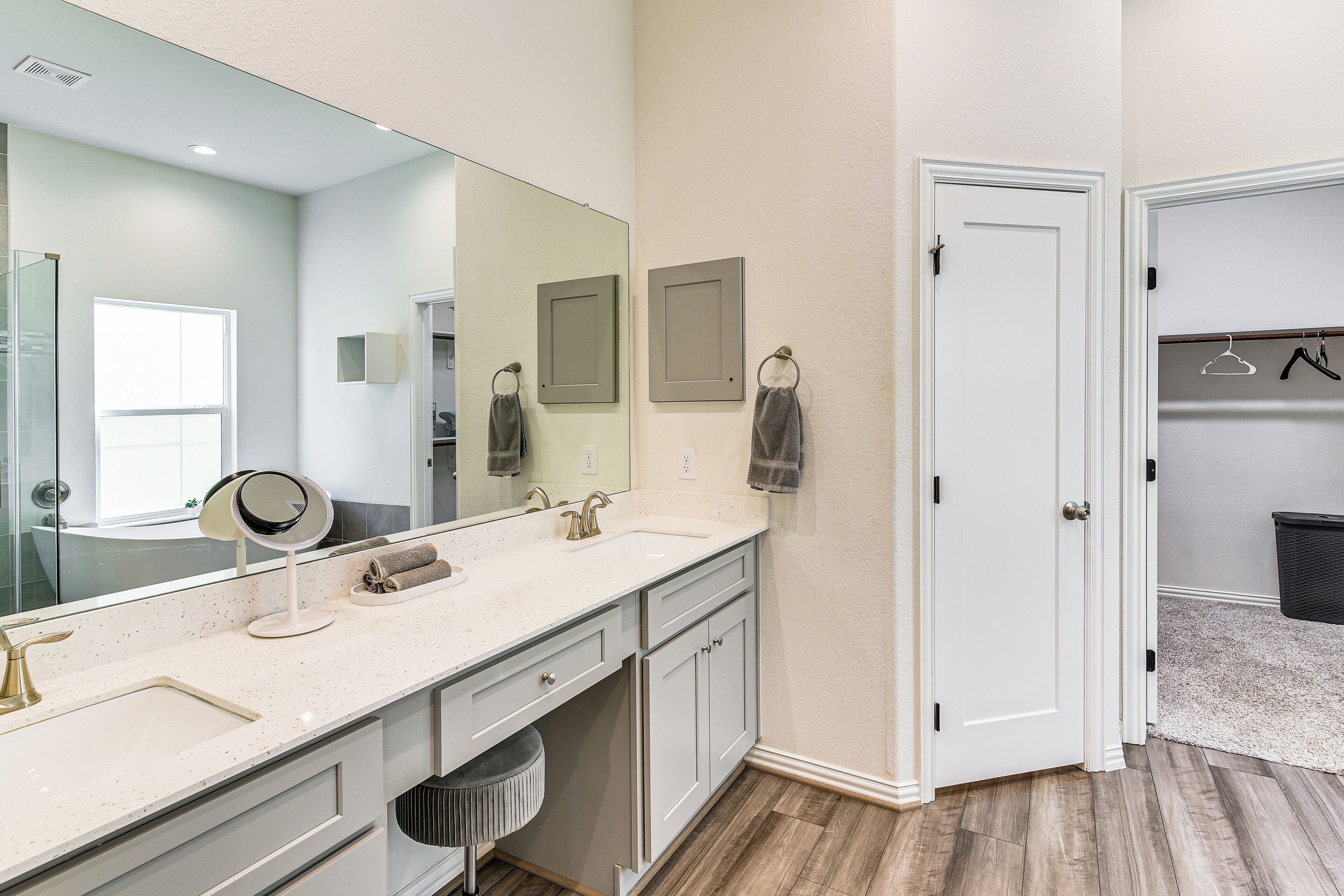 A bathroom with a large mirror, two sinks, a vanity, and a towel rack.