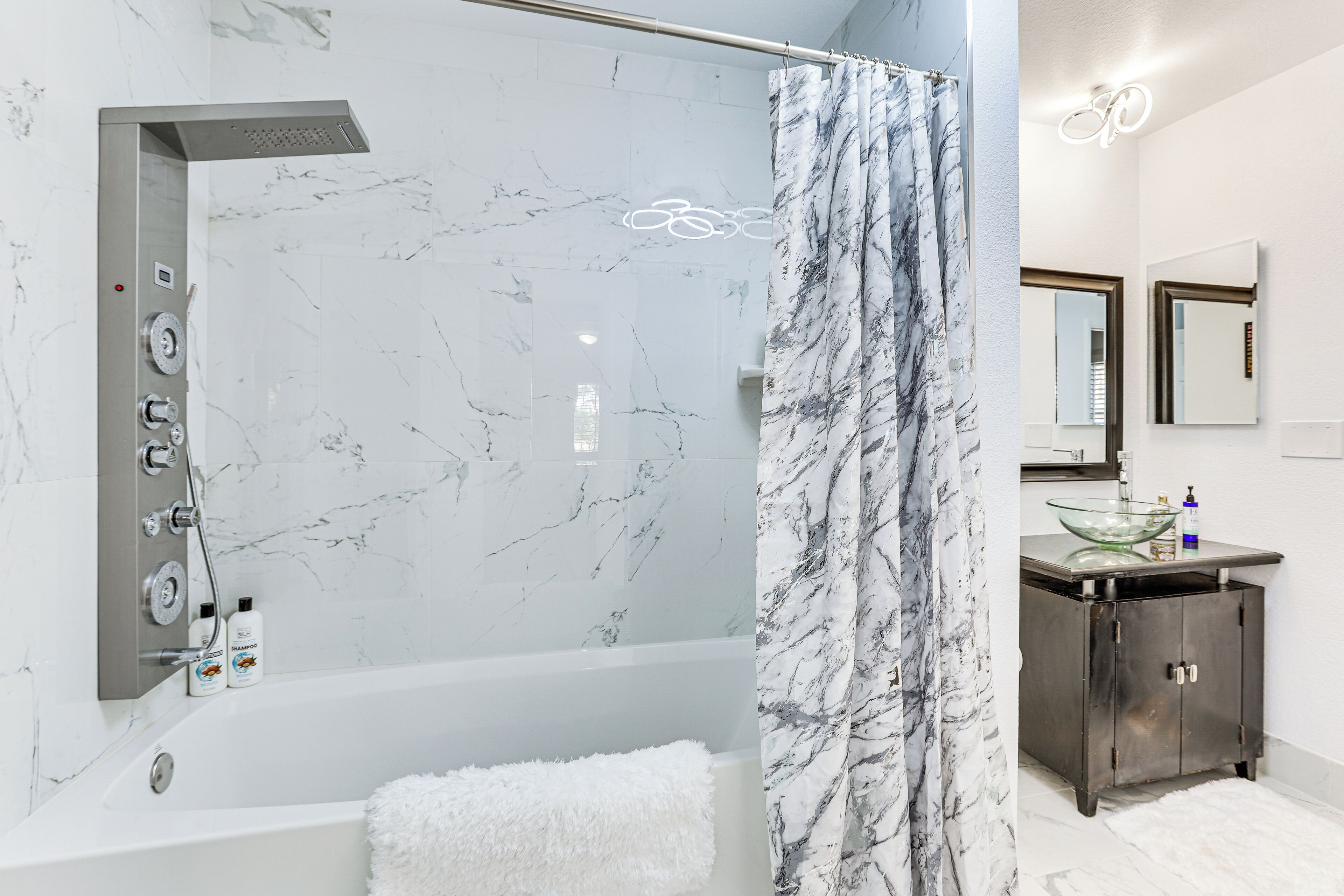 A modern bathroom with a marble shower, a glass-enclosed bathtub, and a dark wooden vanity with a glass bowl sink.