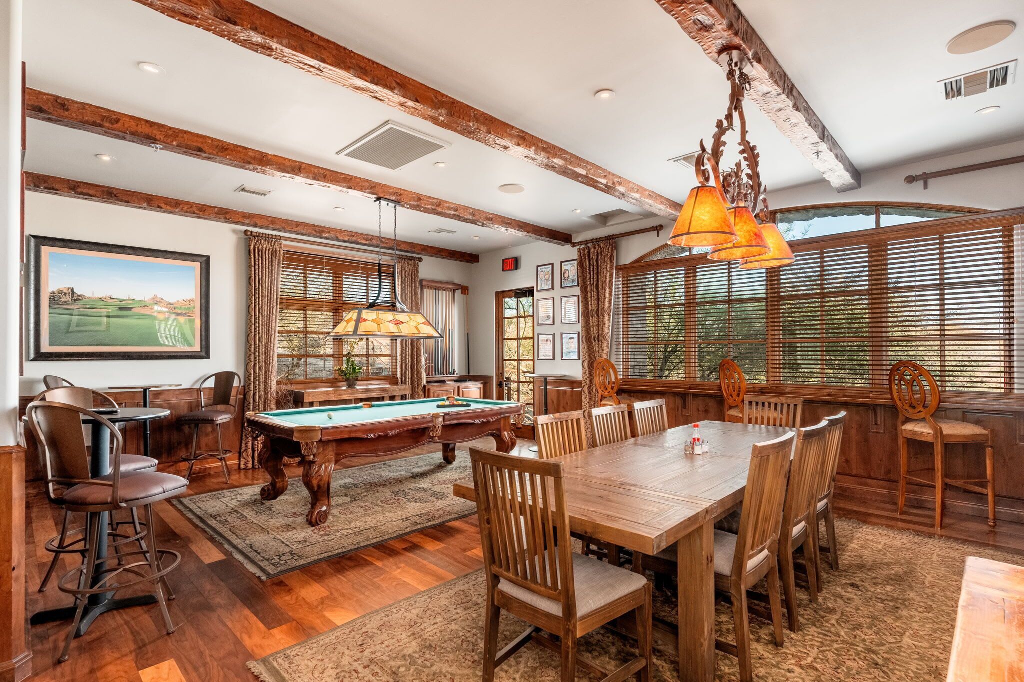 A spacious room with a pool table, wooden dining table, and bar stools.